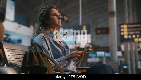 Woman Sits in International Airport Terminal, Using Smartphone Scan QR Code on Boarding Pass. Female Verifies Flight Data While Enjoying Cup of Coffee. Concept of Paperless Travel, Digital Check In. Stock Photo