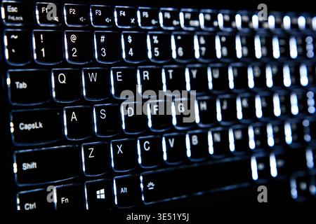 Close-up of a backlit computer keyboard glowing in the dark, QWERTY layout with white LED illumination, concept of gaming, programming, and night work Stock Photo