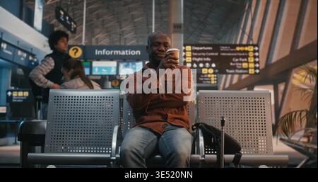 Young Black Man Arrives at Airport Waiting Area, Sets Down Luggage, Immediately Checks Smartphone. Modern Habit of Staying Connected, Checking Flight Updates, Chatting With Friends Before Departure. Stock Photo