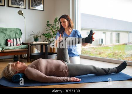 Physiotherapist exercising with older woman during rehabilitation session at home. Stock Photo