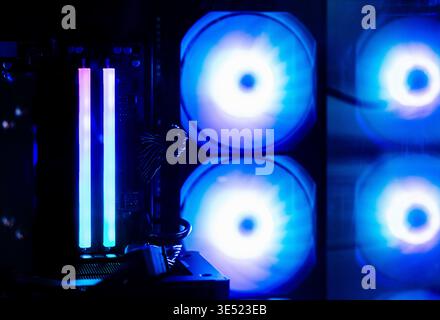 Inside a high-performance gaming PC: a close-up of RAM modules with customizable blue lighting and glowing cooling fans during an esports match. Stock Photo