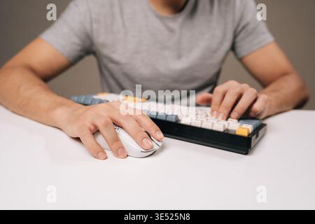 Close-up of male hands typing on colorful mechanical keyboard next to white wireless mouse on clean desk, conveying gaming, coding, remote work, and Stock Photo