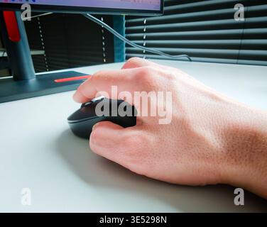 Hand of working person holding computer mouse on desk, office workspace detail with modern technology and everyday productivity concept. Work concept Stock Photo