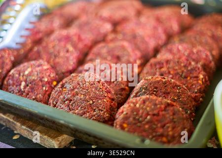 A close-up view of multiple raw meat patties arranged in neat rows inside a rectangular metal or plastic tray. The patties are round, reddish in Stock Photo