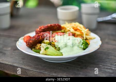 A close-up shot of a white ceramic plate with a decorative gold rim, filled with a colorful vegetarian meal and placed on a weathered dark wooden Stock Photo
