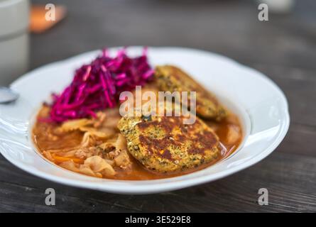 A close-up photograph of a white ceramic bowl filled with a hearty meal, placed on a dark wooden table surface. The dish contains two golden-brown Stock Photo