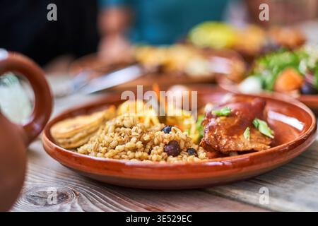A close-up shot of a traditional rustic meal served on a terracotta ceramic plate placed on a wooden table. The dish features seasoned grain or rice Stock Photo
