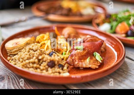 A close-up shot of a rustic meal served on a terracotta plate placed on a wooden table. The dish features a portion of cooked grains mixed with dark Stock Photo