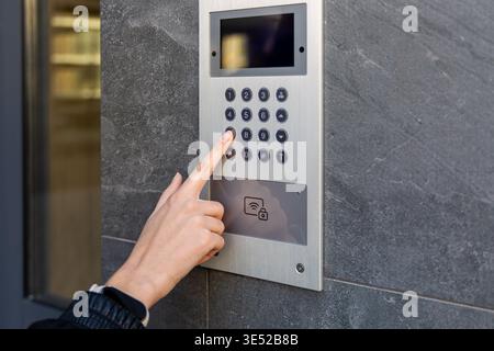 Hand pressing keypad on video intercom panel. Close-up of a hand entering a code on a modern video intercom, showing secure building access, smart Stock Photo