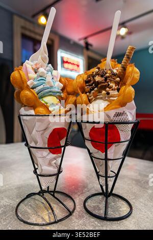 Bubble Waffle Ice Cream Cones in Cafe. Two bubble waffle dessert cones filled with soft serve and toppings on a cafe table, showing a colorful Stock Photo