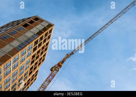 High-Rise Building Under Construction With Tower Crane. Low angle photo of an unfinished high-rise building with a tower crane against blue sky Stock Photo