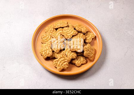 Maple leaf shaped cookies filling an orange ceramic plate, offering a sweet snack or dessert, symbolizing autumn flavors and canadian heritage in a si Stock Photo