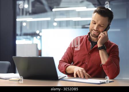 Man Talks on the Phone While Sitting at a Desk With a Laptop in a Modern Office Stock Photo