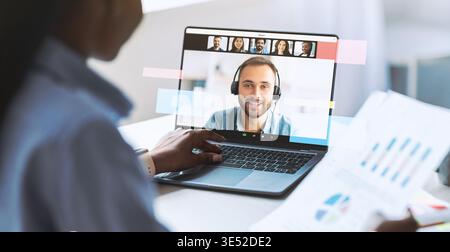 Black Female Employee Working on Laptop and Reviewing Documents at Office Desk During Business Task Stock Photo