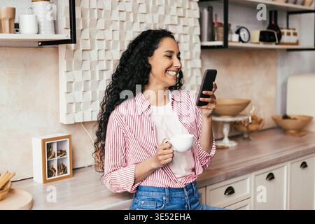 Woman Enjoys Coffee While Using Smartphone in Modern Kitchen Setting Stock Photo
