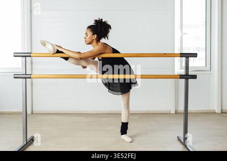 Young ballerina stretching her leg in dance studio. Woman doing exercise on ballet barre Stock Photo