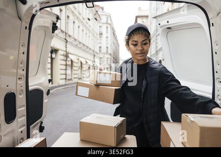 Delivery worker unloading cardboard boxes while standing at van trunk Stock Photo