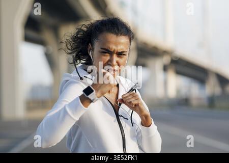 Young sportswoman training boxing moves outdoors. Woman practicing punches at evening on a city street Stock Photo