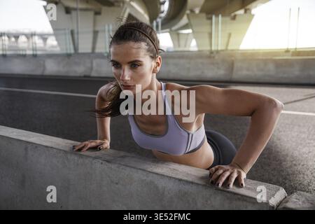 Young woman doing pushups in the street, looking away Stock Photo