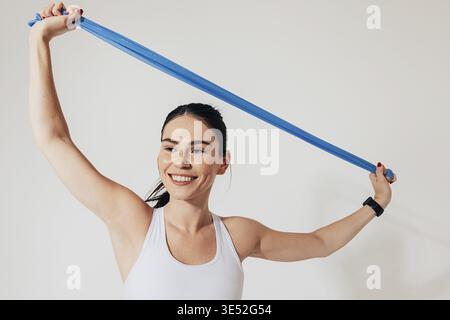 Young smiling woman with resistance band stretching her hands against the white backdrop Stock Photo