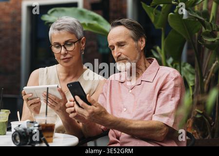 Mature couple using their smartphones while sitting together in an outdoor cafe Stock Photo