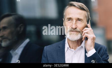 Serious bearded businessman talking on a mobile phone while standing outdoors Stock Photo