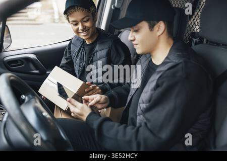 Two couriers in uniform sitting in a van checking delivery information on a digital tablet Stock Photo