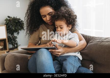Mother and son sitting on the sofa and using digital tablet at home Stock Photo