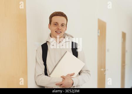 Smiling teenager leaning a wall in high school looking at camera Stock Photo