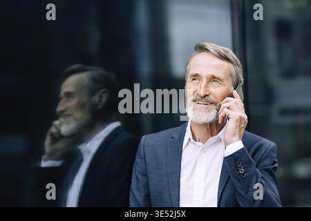 Smiling senior man making call outdoors standing at an office building Stock Photo