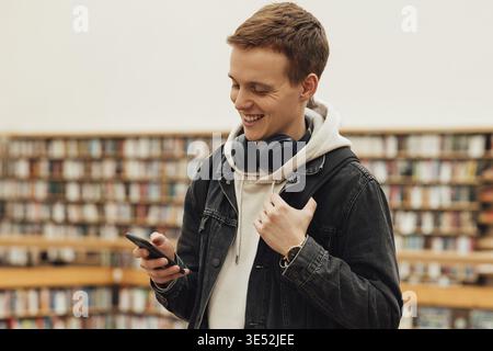 Smiling student using smartphone while standing in library Stock Photo