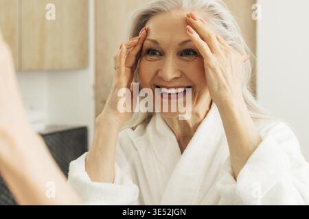 Close up of a happy aged woman touching her face with hands and looking at mirror Stock Photo