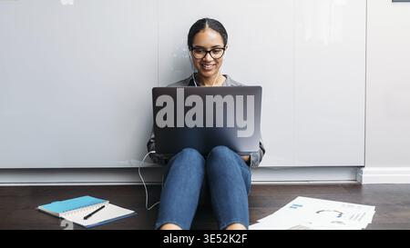Woman video calling on the kitchen floor. Smiling entrepreneur working on laptop Stock Photo