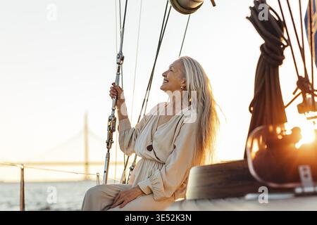 Side view of mature woman with long hair sitting on yacht and smiling Stock Photo