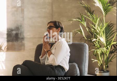 Side view of a middle-aged woman in formal wear sitting indoors and talking on a mobile phone Stock Photo