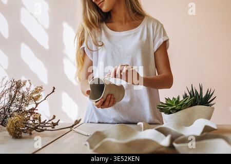 Young ceramic artist working in her studio. Female potter finishing a clay mug Stock Photo
