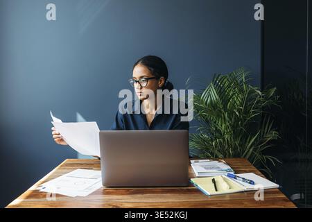 Serious businesswoman sitting by a desk and holds documents Stock Photo