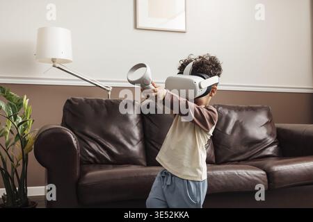 Kid playing virtual reality game in a living room holding joystick with two hands Stock Photo