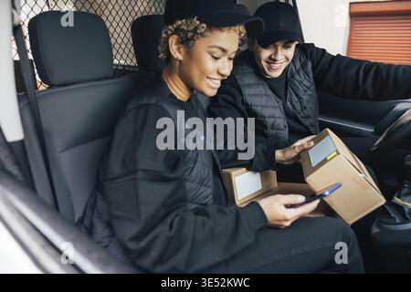 Two couriers sitting in car checking information on box using mobile phone Stock Photo