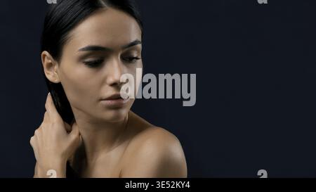 Beautiful woman holding her black hair, studio portrait against dark backdrop Stock Photo