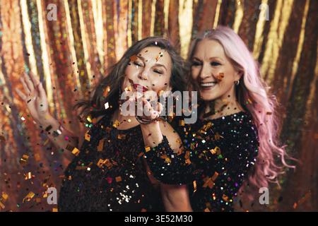 Two senior girlfriends having fun in studio blowing confetti Stock Photo