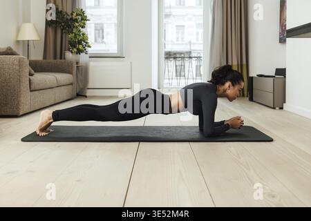 Side view of a slim woman in sportswear doing plank at home Stock Photo
