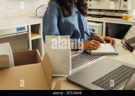Mid section of businesswoman in her small cafe writing on notebook. Entrepreneur preparing packs of coffee for shipment Stock Photo