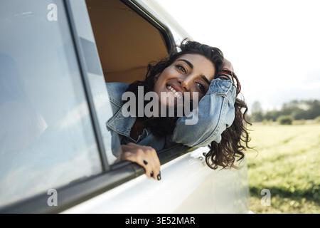 Attractive young woman enjoying road trip. Smiling female looks out Stock Photo