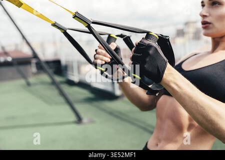Sporty young woman doing exercises with suspension straps on roof terrace Stock Photo