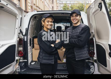 Portrait of a two confident and smiling couriers standing together at van trunk Stock Photo