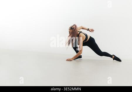 Young woman in sports clothes doing warming up jumps indoors. Athlete preparing for training Stock Photo