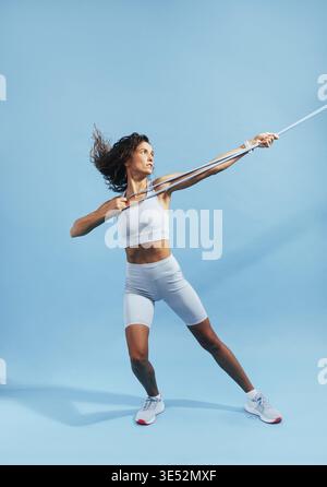 Full length of a slim woman in sportswear practicing on blue background with a resistance band Stock Photo