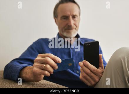 Close up of hands of a senior man holding a smartphone and credit card while sitting Stock Photo