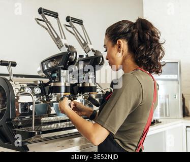 Female barista using a coffee machine to make an espresso. Young cafe worker preparing a beverage Stock Photo